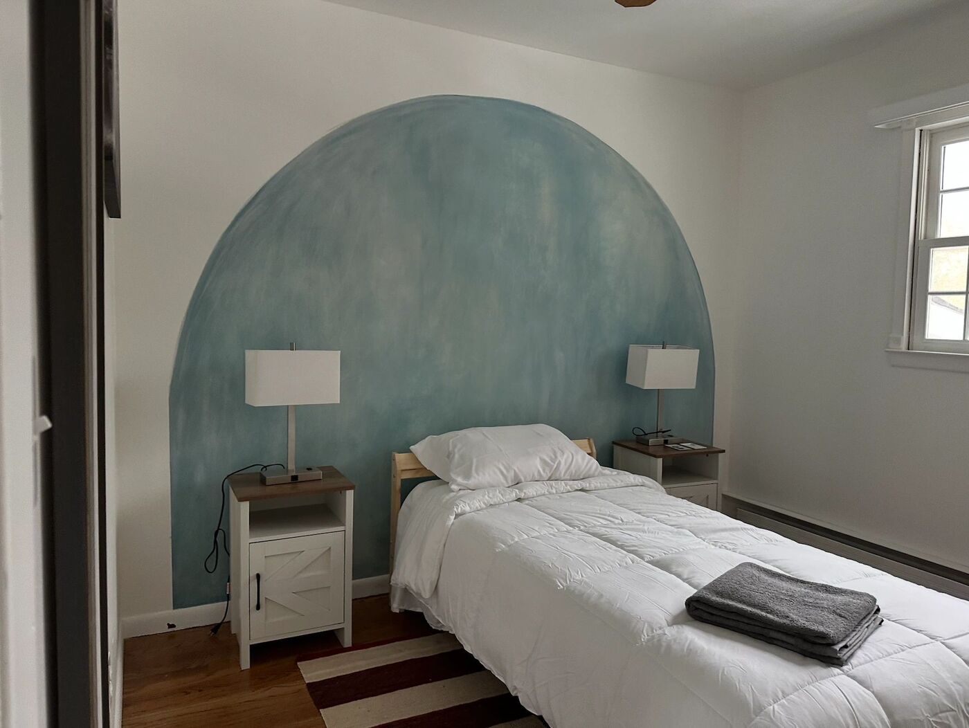 A bedroom with a single bed and a painted blue arch on the wall.